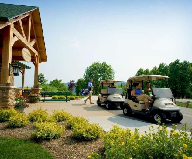 Several people with golf carts are outside a building surrounded by greenery and flowers, creating a picturesque and serene setting.