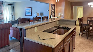 A spacious open-plan kitchen and living area with an island, dining table, seating, and soft lighting in neutral tones.