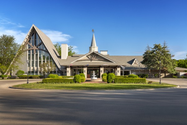 A church with a distinctive triangular glass facade, a tall steeple, well-kept shrubs, and a circular driveway in front of the entrance.