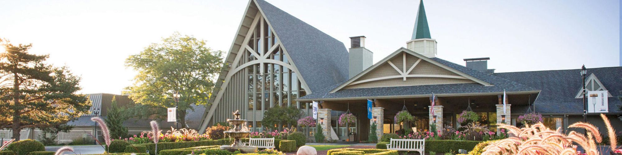A charming building with a tall triangular roof, surrounded by lush gardens and vibrant flowers, under a clear sky during daylight.