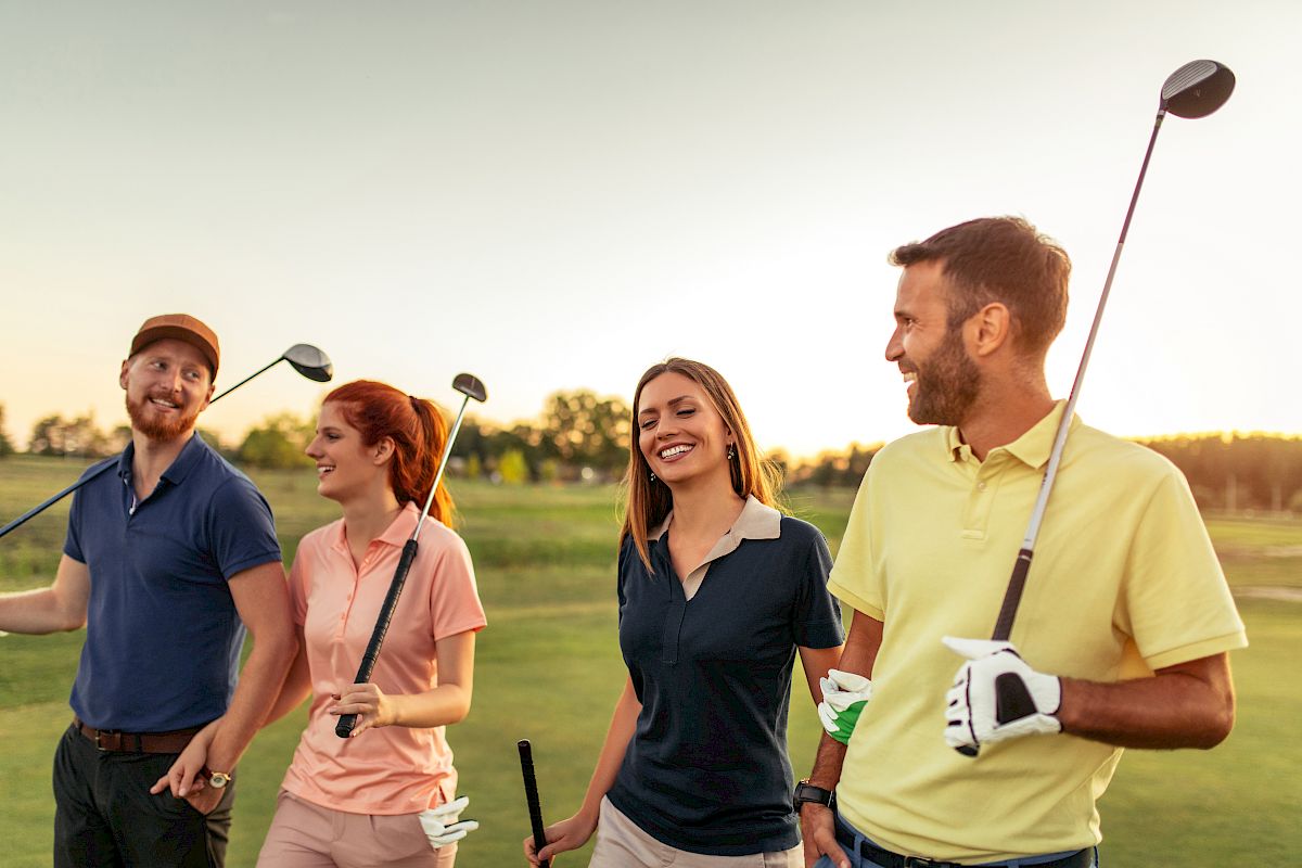 A group of four people are walking on a golf course, each holding a golf club, and enjoying their time outdoors together under a clear sky.