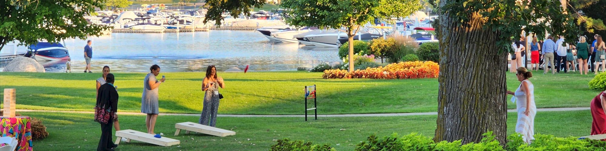 People are enjoying a lakeside gathering with various activities, including playing games and socializing on a lush green lawn.