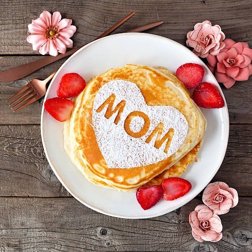 A stack of pancakes with a heart-shaped powder sugar design and the word 