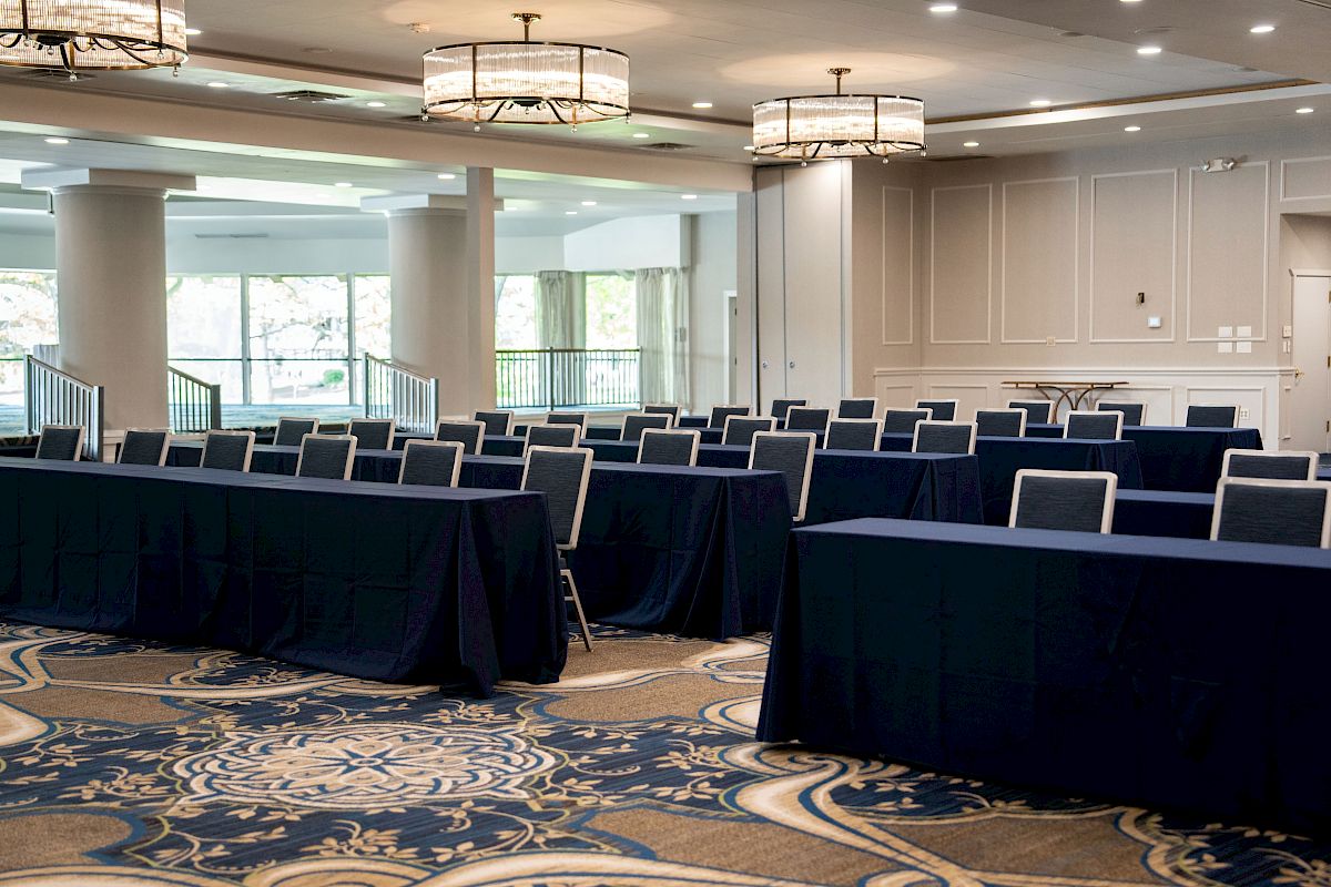 The image shows a conference room setup with rows of tables and chairs, elegant lighting, and a patterned carpet.