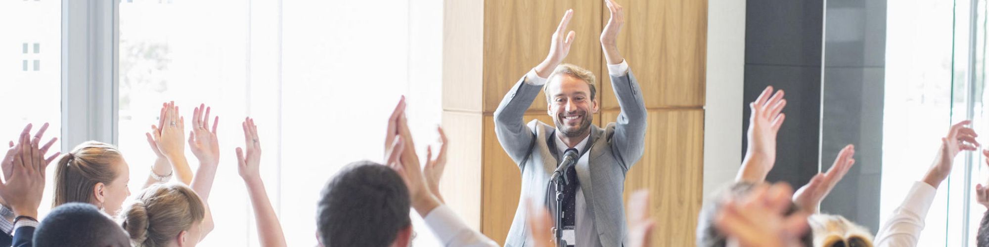 A group of people are standing and clapping with their hands raised while a man in the front leads the activity, also clapping with a smile.