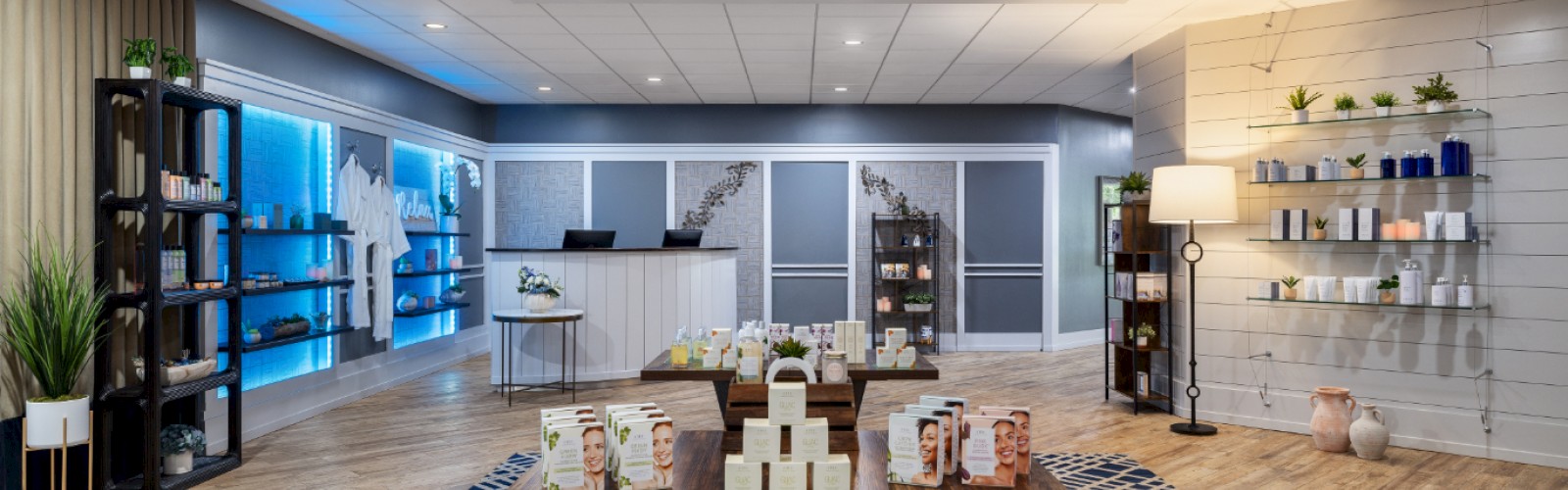 The image shows a modern retail space with shelves and a display table featuring various products, set on a patterned rug.