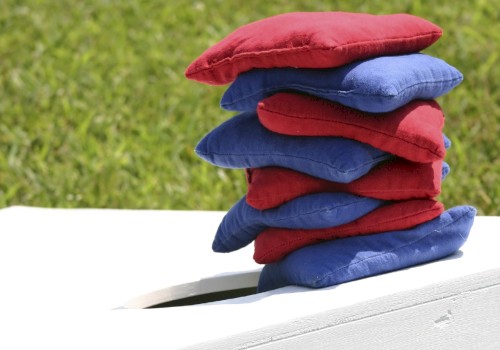 A stack of red and blue cushions is arranged on a white bench outdoors near green grass, creating a colorful and cozy display.