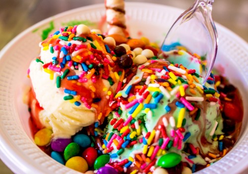 A bowl of ice cream topped with colorful sprinkles, candies, and syrup with a spoon inside it.