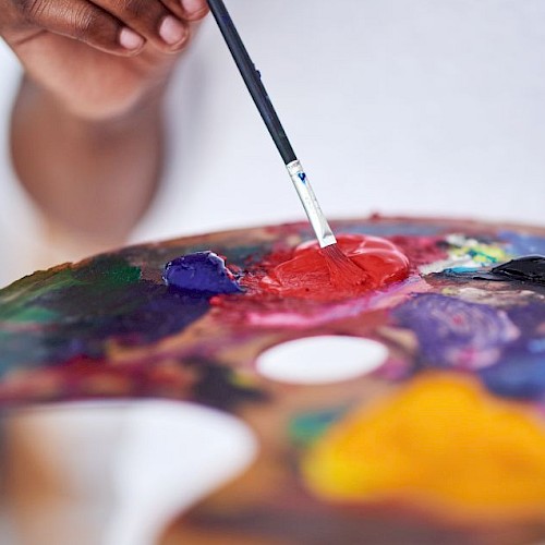 Someone is mixing vibrant paint colors on a palette using a brush, likely preparing to create a colorful artwork.
