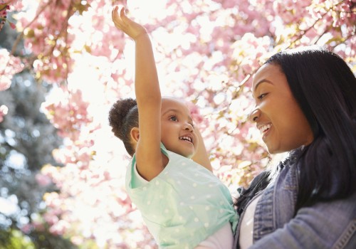 A woman holding a smiling girl under blooming pink cherry blossom trees.