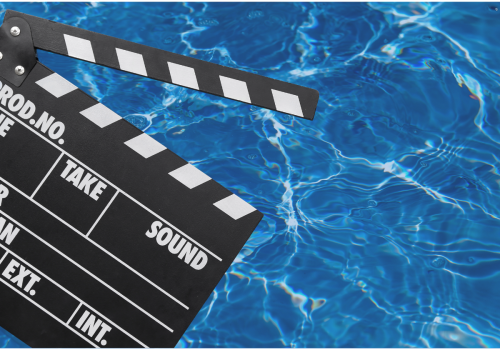 A film clapperboard is floating on a blue, rippling water surface, likely on a swimming pool.