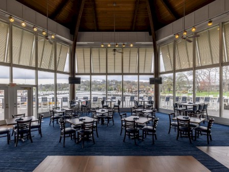 A bright, spacious restaurant with large windows overlooking a lake, furnished with dark wood tables and chairs.
