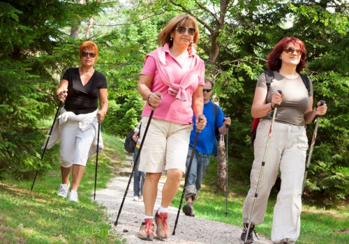 A group of women and a man hiking outdoors on a trail surrounded by trees and lush greenery.