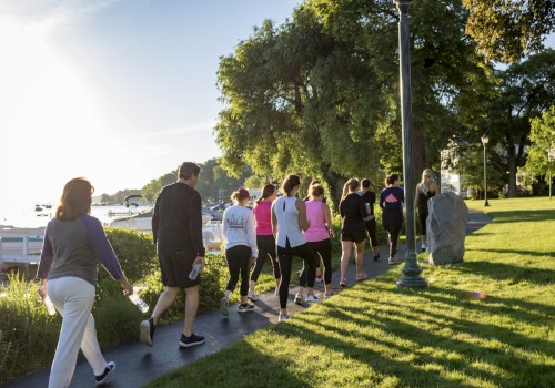 A group of people are jogging along a scenic lakeside path in the early morning, surrounded by trees and lush greenery.