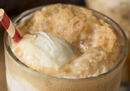 A close-up of a glass filled with a caramel-colored whipped beverage topped with a scoop of vanilla ice cream and a striped straw.