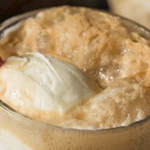 A close-up of a glass filled with a caramel-colored whipped beverage topped with a scoop of vanilla ice cream and a striped straw.