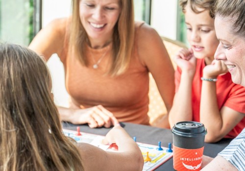 A woman and two children are playing a game of Monopoly while smiling and enjoying each other's company at a table.