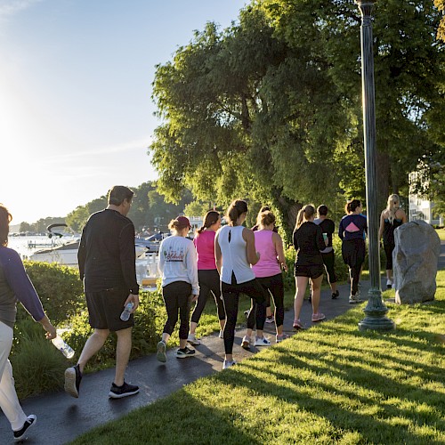 A group of people are jogging along a scenic lakeside path in the early morning, surrounded by trees and lush greenery.