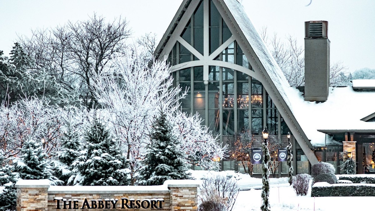 A snowy view of The Abbey Resort with snow-covered trees and a modern A-frame building in the background.