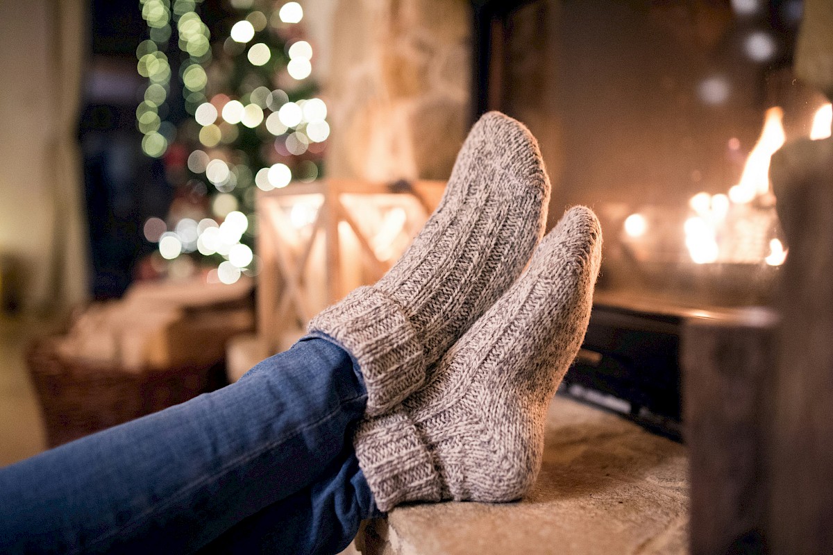 Person relaxing by a cozy fireplace during Christmas, with festive lights and decorated tree in the background.