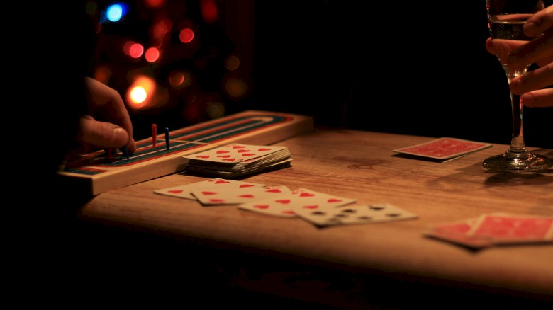 People playing a card game at a wooden table with a glass of champagne, illuminated by dim, warm lighting.
