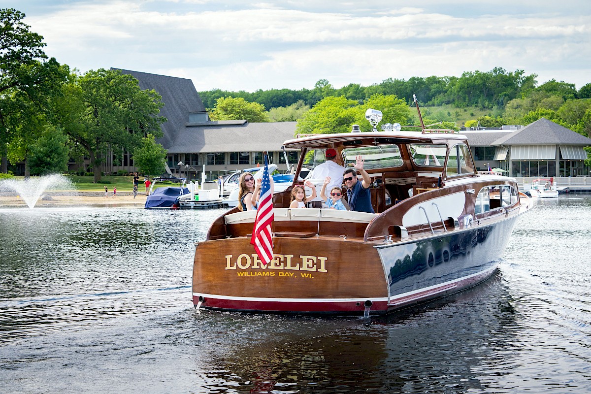 A family enjoys a boat ride on a marina in Wisconsin, with boats, water, and green trees in the background.