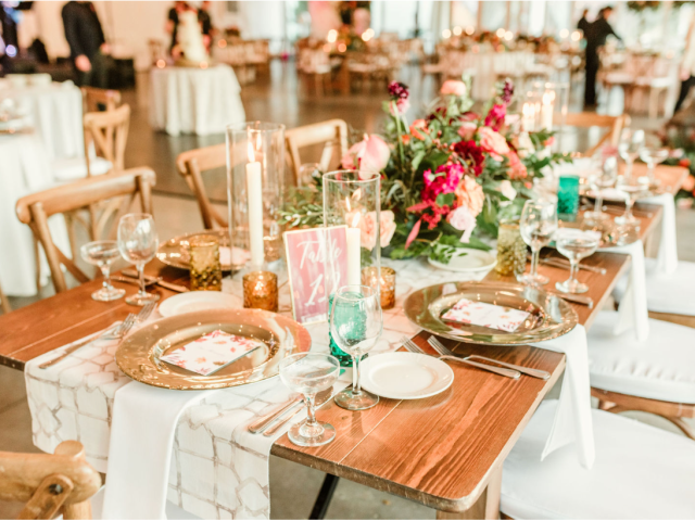 A beautifully decorated dining table with floral centerpieces, candles, plates, glasses, and cutlery. The setting suggests a formal event.