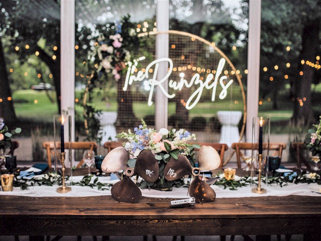The image shows an elegantly decorated wedding reception table with flowers, candles, and a personalized sign reading 