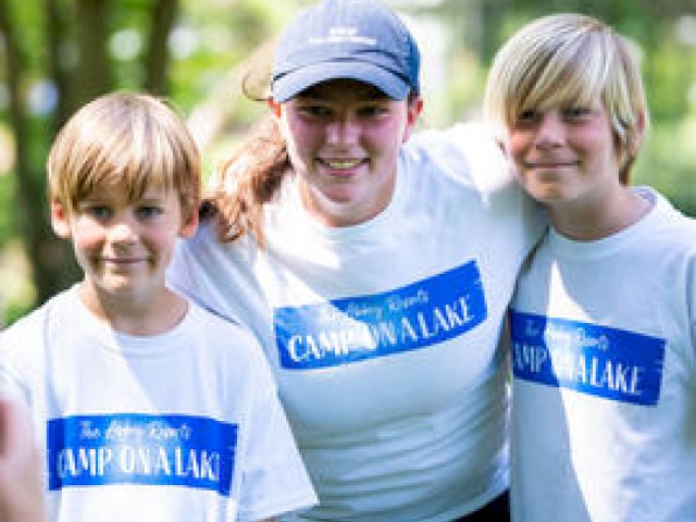Three people are smiling outdoors, wearing matching 