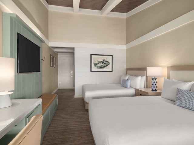 The image shows a hotel room with two beds, a TV, and a desk lamp, featuring minimalistic decor and soft lighting for a cozy ambiance.