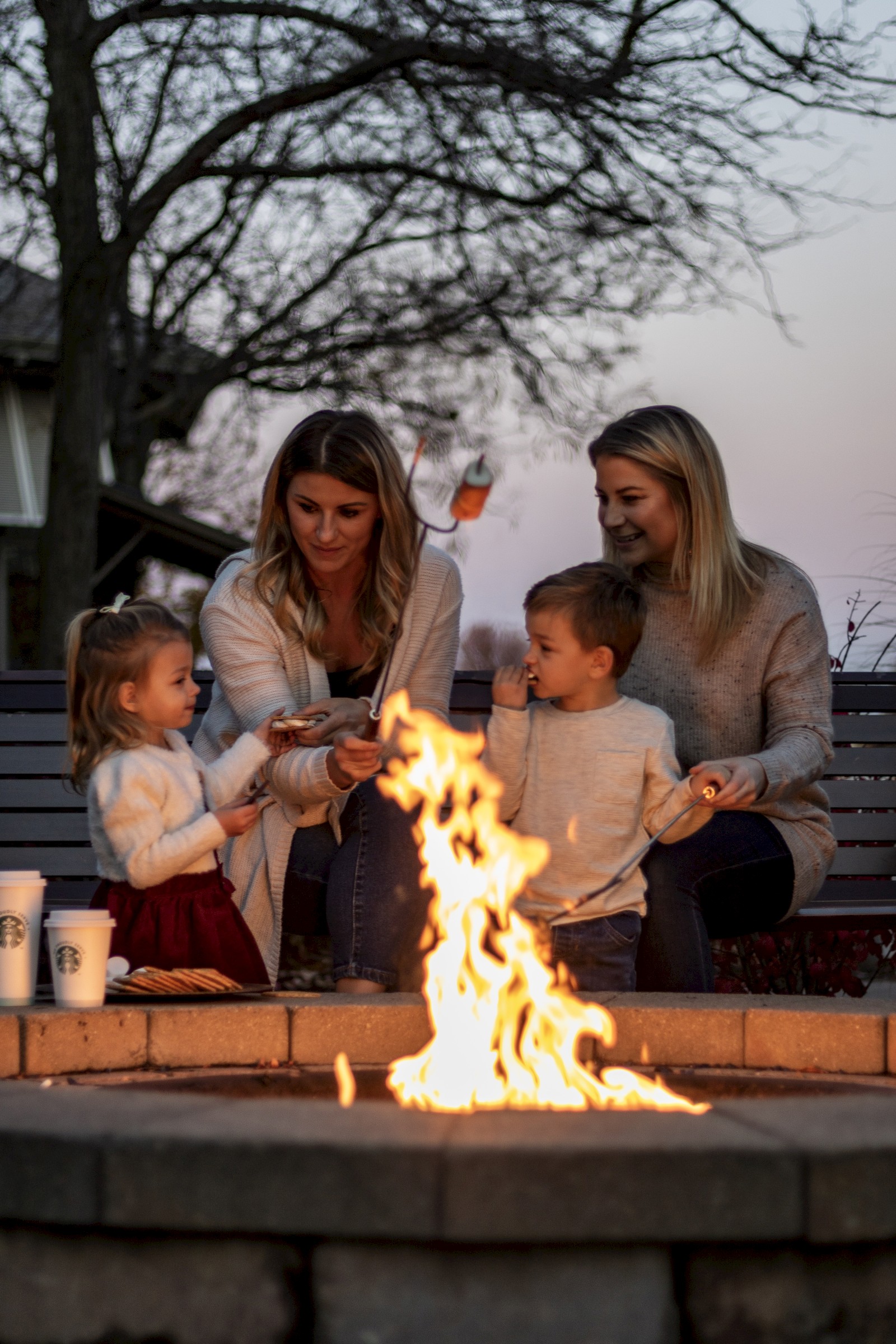 A family gathers around a backyard fire pit, roasting marshmallows together on a chilly evening.
