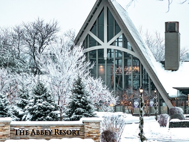A snow-covered building with a tall, triangular glass front, surrounded by snowy trees and a sign that reads 