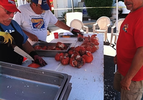 Three men prepare and cook pumpkins outdoors, with one slicing, another cutting, and a third overseeing the pumpkin pile on the table.