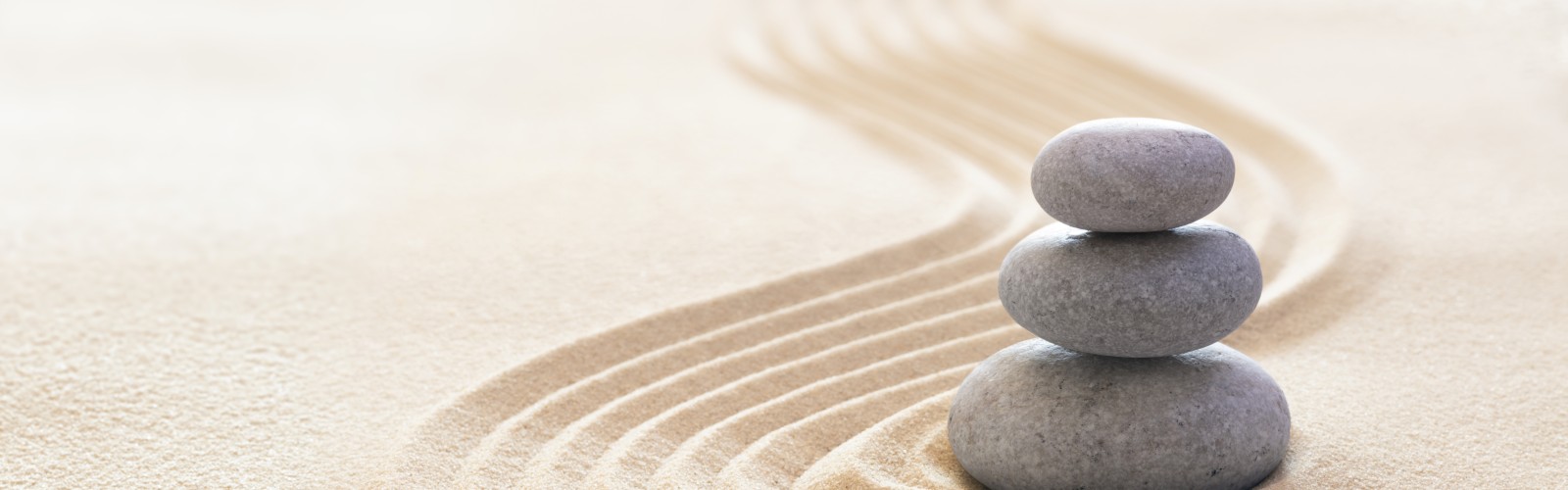 Three smooth stones stacked on sand with curved lines drawn around them, creating a calm and minimalistic Zen garden scene.