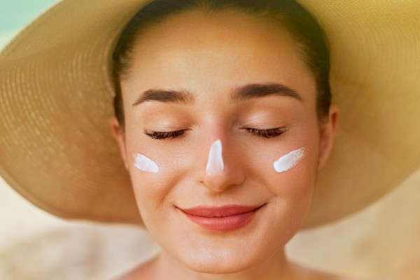 A person with a sun hat and sunscreen on their face, smiling with closed eyes.