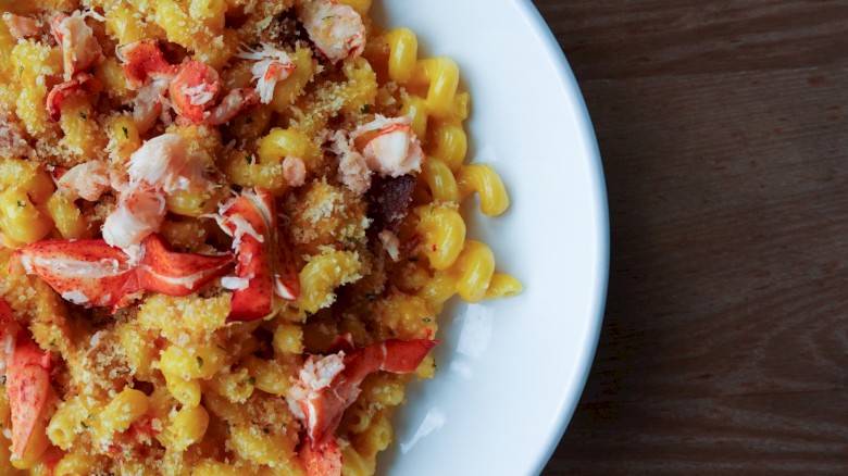 A plate of pasta with lobster and a crumbly topping, served on a white dish against a wooden table background.