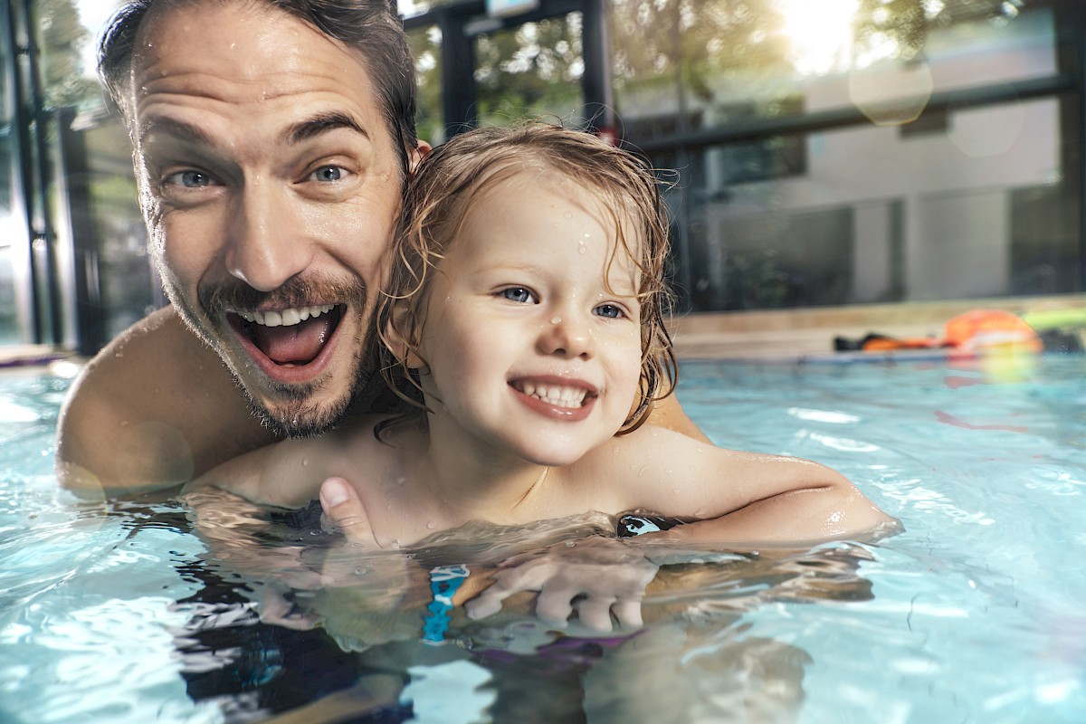 A smiling man and child are enjoying time together in a swimming pool, splashing around with joy and laughter.