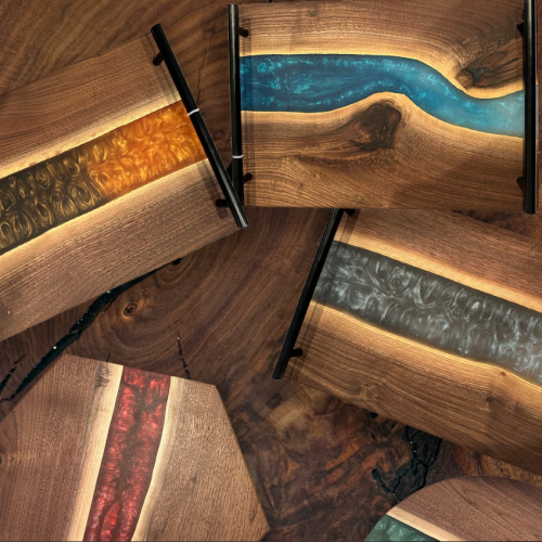 This image features five wooden trays with colorful resin inlays in various patterns, laying on top of a wooden surface.