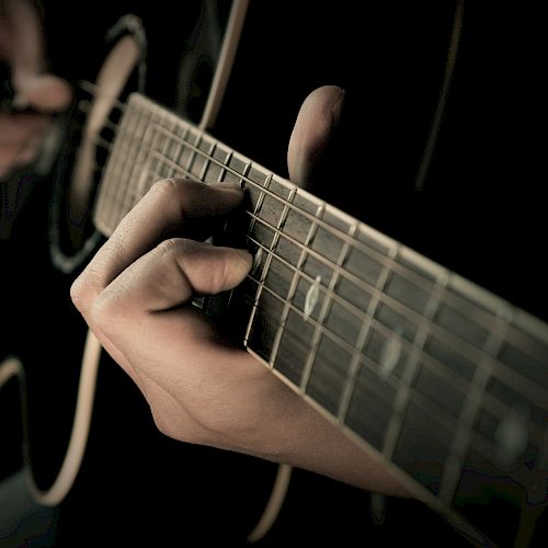 A close-up image of a person playing an acoustic guitar, showing their hands pressing the strings along the fretboard.