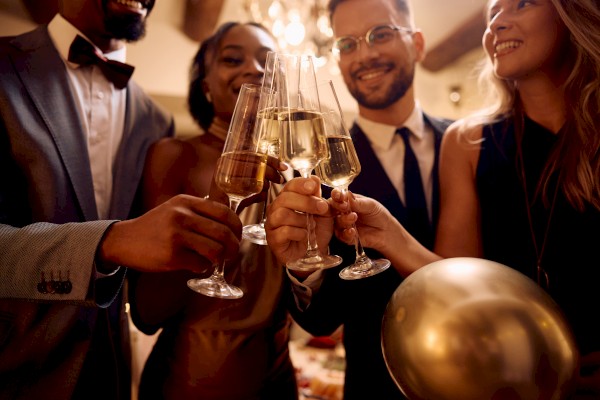 A group of people dressed formally, holding champagne glasses, toasting together at a celebration, with one person holding a gold balloon.