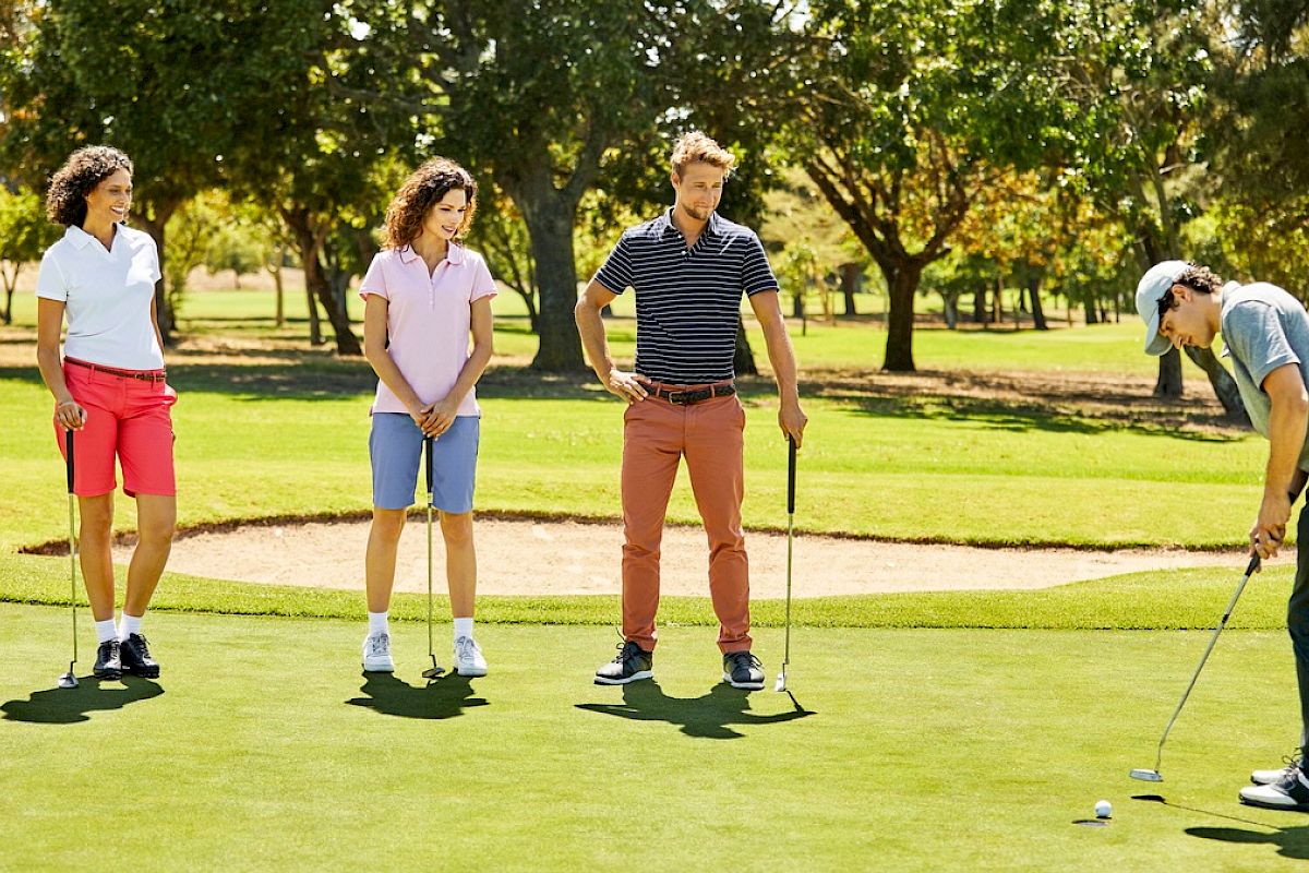 Four people are on a golf course; three are watching while one is putting the golf ball.