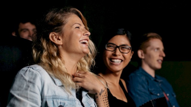 Three people are sitting and laughing, likely enjoying a movie or performance together.