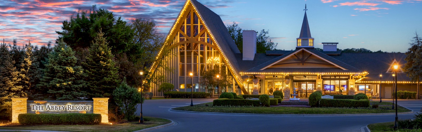 The Abbey Resort, a charming lakeside hotel, is beautifully lit at dusk with colorful clouds in the sky.