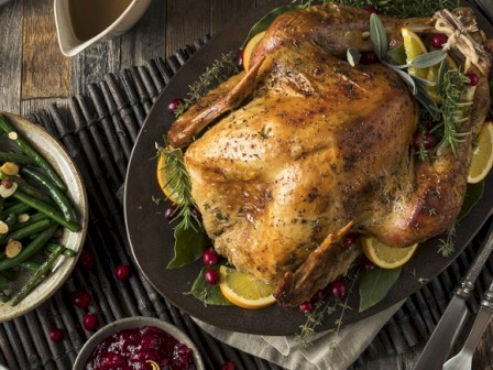 The image shows a festive meal with a roasted turkey, cranberry sauce, green beans, Brussels sprouts, gravy, and other side dishes on a rustic table.