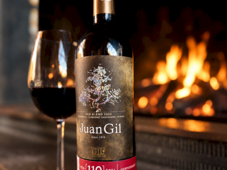 Bottle of Juan Gil red wine and a glass of wine in front of a fireplace, celebrating the winery's 110th anniversary.