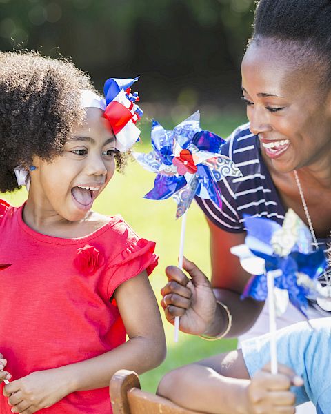A joyful group of three people play outdoors with colorful pinwheels, enjoying their time together in a sunny park setting.