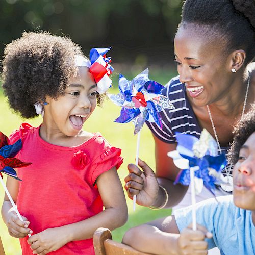 A joyful group of three people play outdoors with colorful pinwheels, enjoying their time together in a sunny park setting.