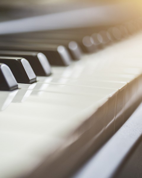 A close-up of piano keys with soft lighting highlighting the keys from the upper right corner, creating a warm and inviting atmosphere.