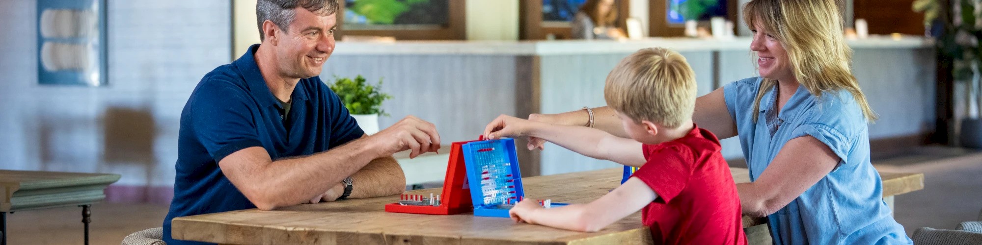 A family of three is gathered around a table playing a board game with smiles, enjoying their time together indoors.