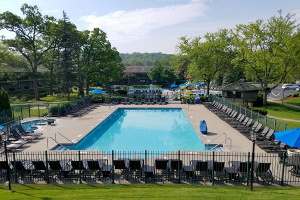 An outdoor pool area surrounded by lounge chairs and trees, with a fenced-in pool and a pathway leading to more seating and structures.